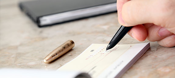 An older woman writing a check to make either a one time or recurring tax-deductible donation to help spread God's word.